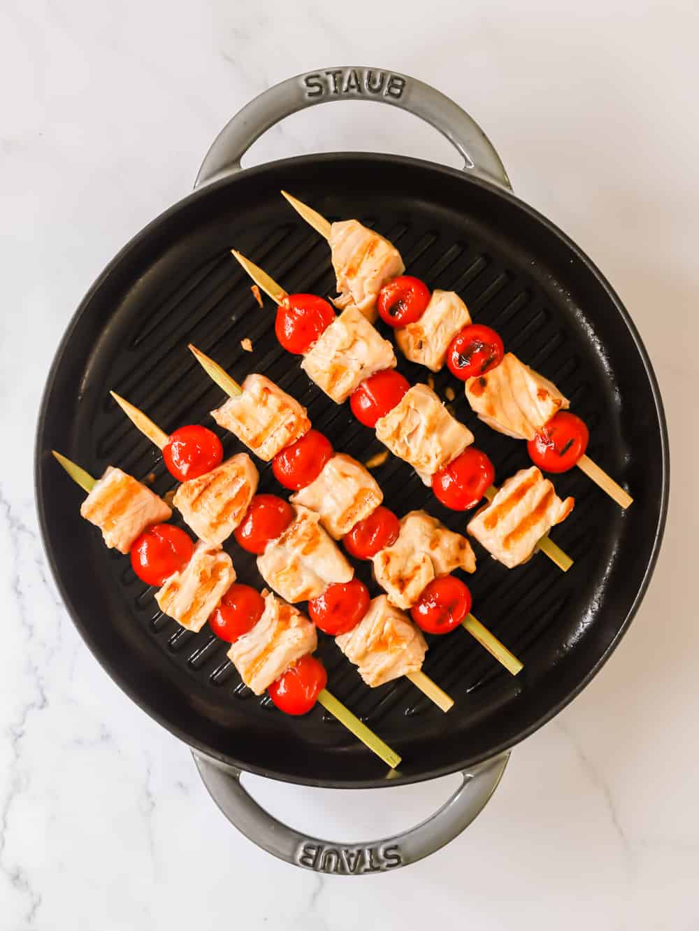Enjoy these Grilled Salmon Kabobs for a quick and easy lunch or dinner. Juicy salmon and tomatoes are threaded onto skewers before being grilled to perfection and topped with chimichurri sauce. It’s a simple, yet flavor-packed meal! #salmonkabobs #summerrecipe #grilling #grilledsalmon #kabobs grilled salmon and tomato skewers on a large black skillet.