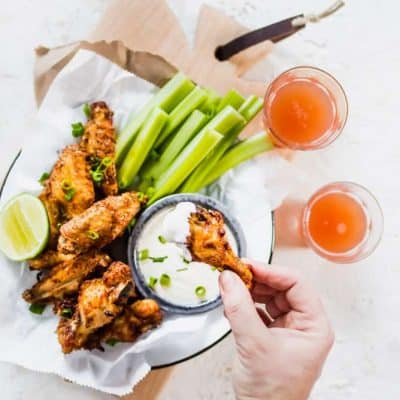 Extra Crispy Air Fryer Wings with celery and homemade ranch sauce on plate being picked up with hand. lenaskitchenblog.com