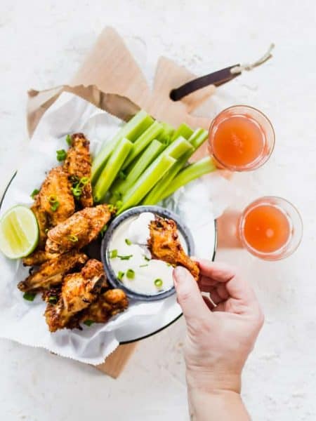 Extra Crispy Air Fryer Wings with celery and homemade ranch sauce on plate being picked up with hand. lenaskitchenblog.com