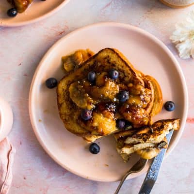 Cooked french toast on a pink plate with a fork and knife
