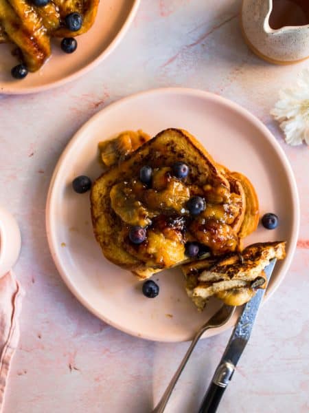 Cooked french toast on a pink plate with a fork and knife