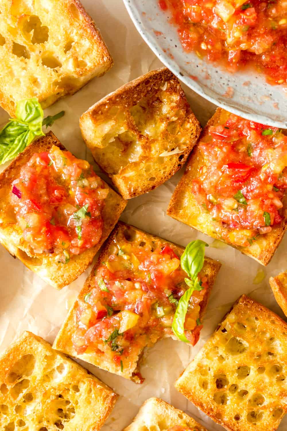 close up on pieces of Spanish tomato bread next to a bowl filled with a crushed tomato and herb sauce.