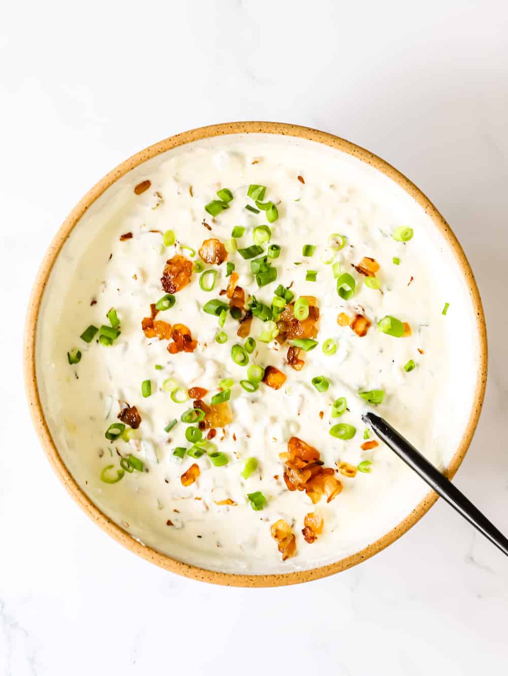 A bowl filled with creamy onion dip topped with caramelized onions and green onions.