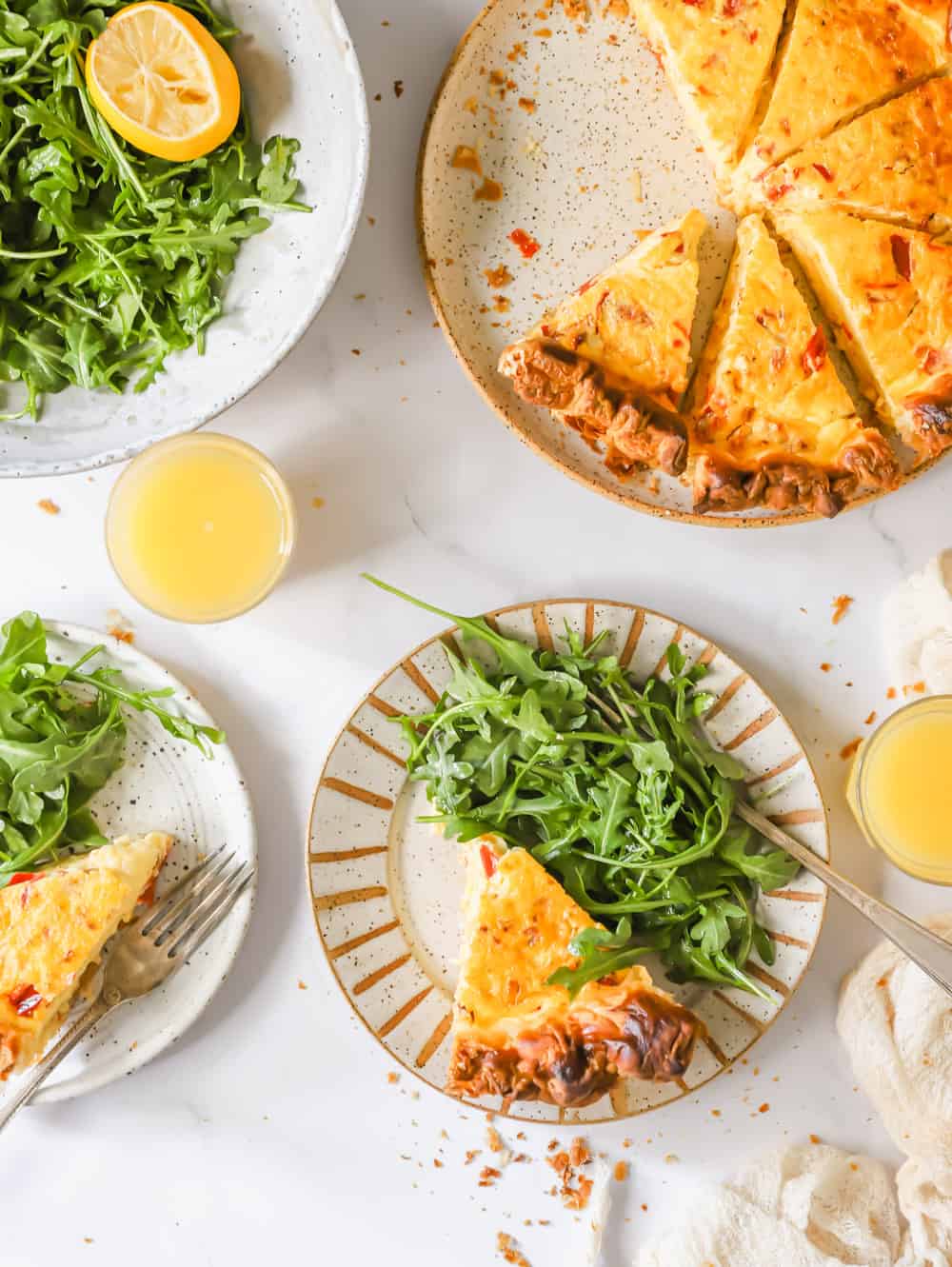 Individual servings of quiche and salad on white plates next to a larger, sliced quiche.