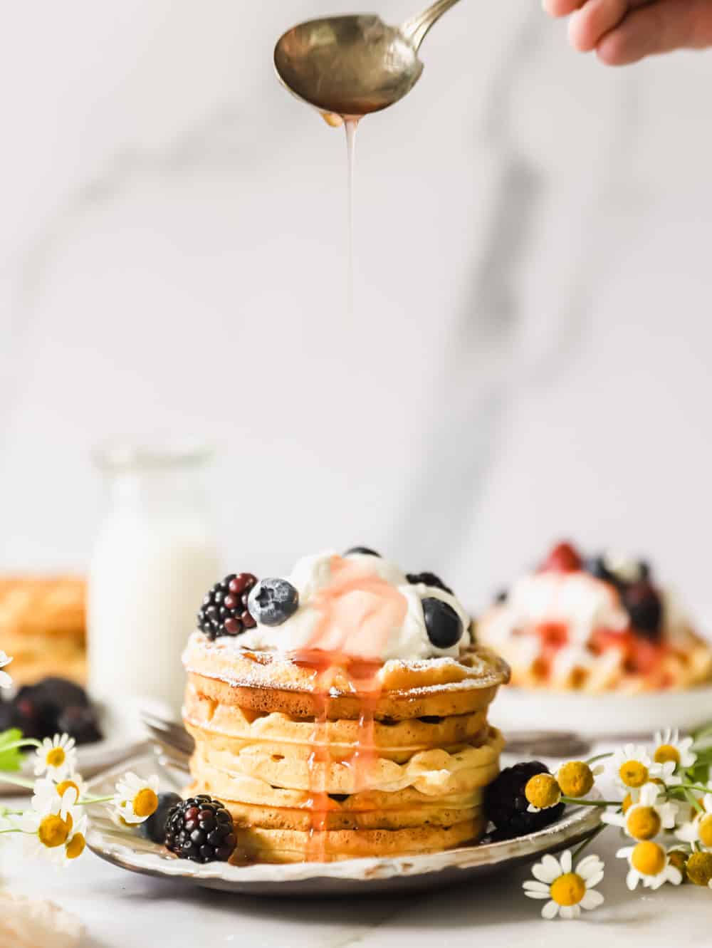 a stack of buttermilk waffles topped with whipped cream and berries on a plate.