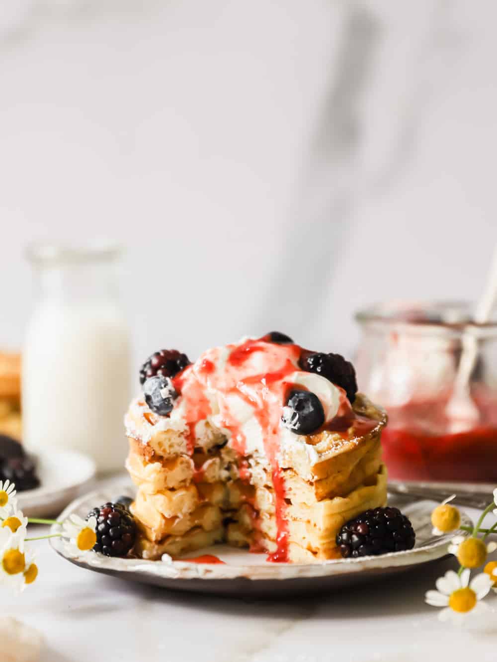 a stack of buttermilk waffles topped with whipped cream and berries on a plate.