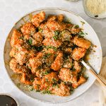 Overhead shot of honey sesame chicken in a serving bowl with chopped green onions and sesame seeds on the side.