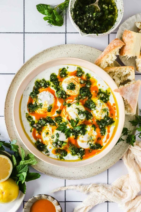 Overhead shot of Turkish eggs with crusty bread and chimichurri sauce on the side.