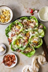 A plate of butter lettuce cups filled with grilled corn, sliced radishes, prosciutto bits, shredded cheese, and creamy dressing.