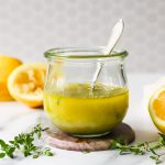 A glass jar filled with lemon vinaigrette dressing with a spoon inside.