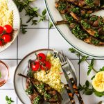 Overhead shot of Greek lamb chops being served in a plate with cherry tomatoes and rice. More lamb chops in a bigger serving dish.