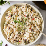 A bowl of chicken salad garnished with herbs sits on a table, surrounded by bread, fresh greens, and cranberries. Text above reads "Chicken Salad Recipe - Great for Leftover Chicken.