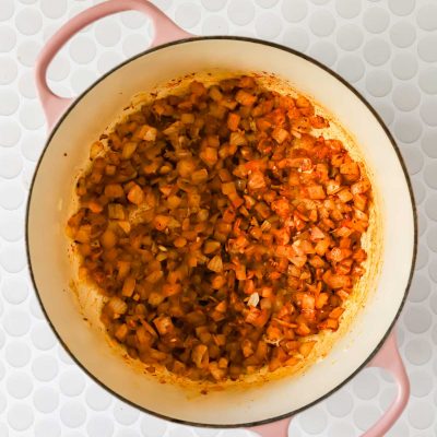 Diced onions saut&eacute;ed with spices in a large cream and pink pot, placed on a white circular-tile surface.