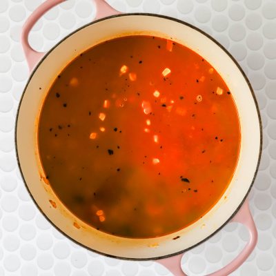 A pot of chicken poblano soup with herbs, viewed from above, on a white textured surface.