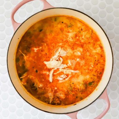 Large pot filled with chicken poblano soup, shredded chicken, and herbs on a white patterned surface.
