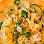 A bowl of chicken poblano soup with shredded chicken, corn, tortilla chips, cilantro, and a creamy broth, served with a spoon.