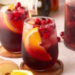 A glass with fall sangria with cranberries and sliced oranges, with more in the back.