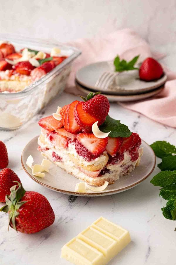 A plate with a serving of strawberry tiramisu, with more in the background.