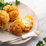 Three cheddar bay biscuits on a plate, one split open with butter melting inside. A butter knife with butter rests on the plate, garnished with parsley.