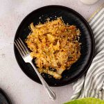 A black plate with cooked cabbage topped with breadcrumbs, a fork on the side, and a striped napkin nearby.