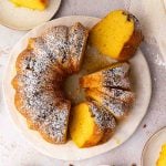 A rum cake dusted with powdered sugar, partially sliced on a white plate, with a few slices cut and separated from the whole cake.