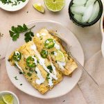Green chicken enchiladas in a plate with a fork on the side.
