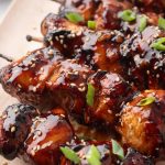 Close-up of glazed chicken skewers topped with sesame seeds and chopped green onions, arranged on a tray. Text reads "Sweet and Savory Air Fryer Chicken Skewers - LenasKitchenBlog.com.