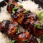 Two glazed chicken skewers garnished with green onions and sesame seeds served over white rice, labeled as Asian Style Air Fryer Chicken Skewers.