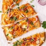Sliced buffalo chicken flatbread topped with red onion, green onions, and fresh herbs, served on parchment paper with celery and carrot sticks on the side.