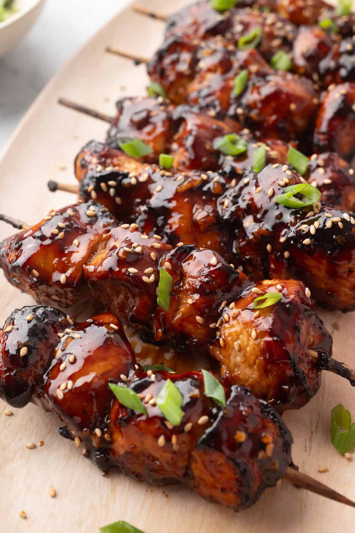 Air fried chicken skewers coated in a glossy sauce, garnished with sesame seeds and chopped green onions, arranged on a light wooden surface.