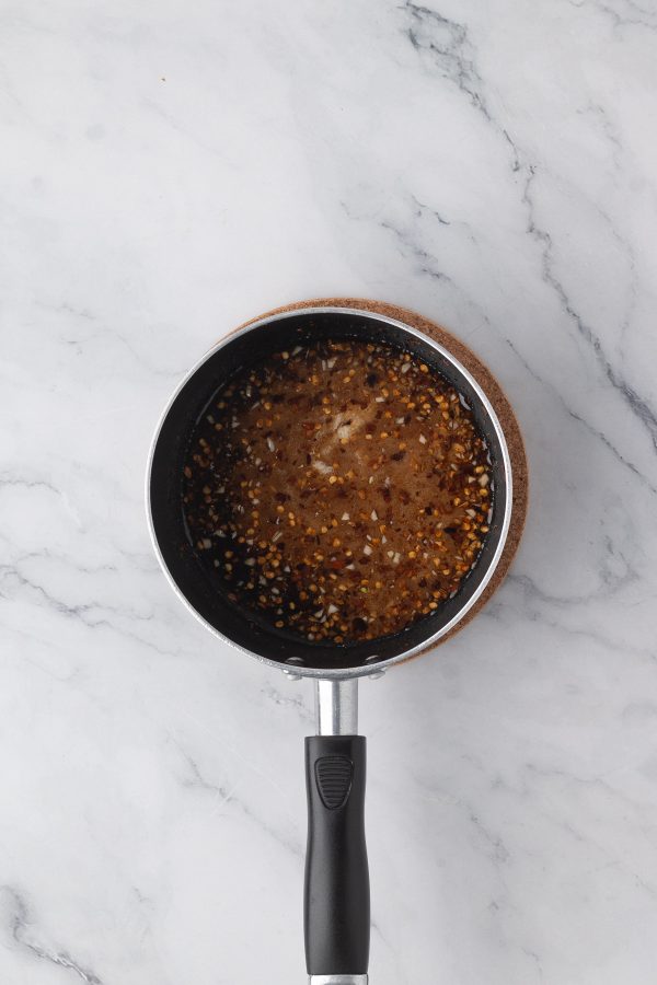 A small saucepan filled with a dark, chunky sauce sits on a marble countertop.