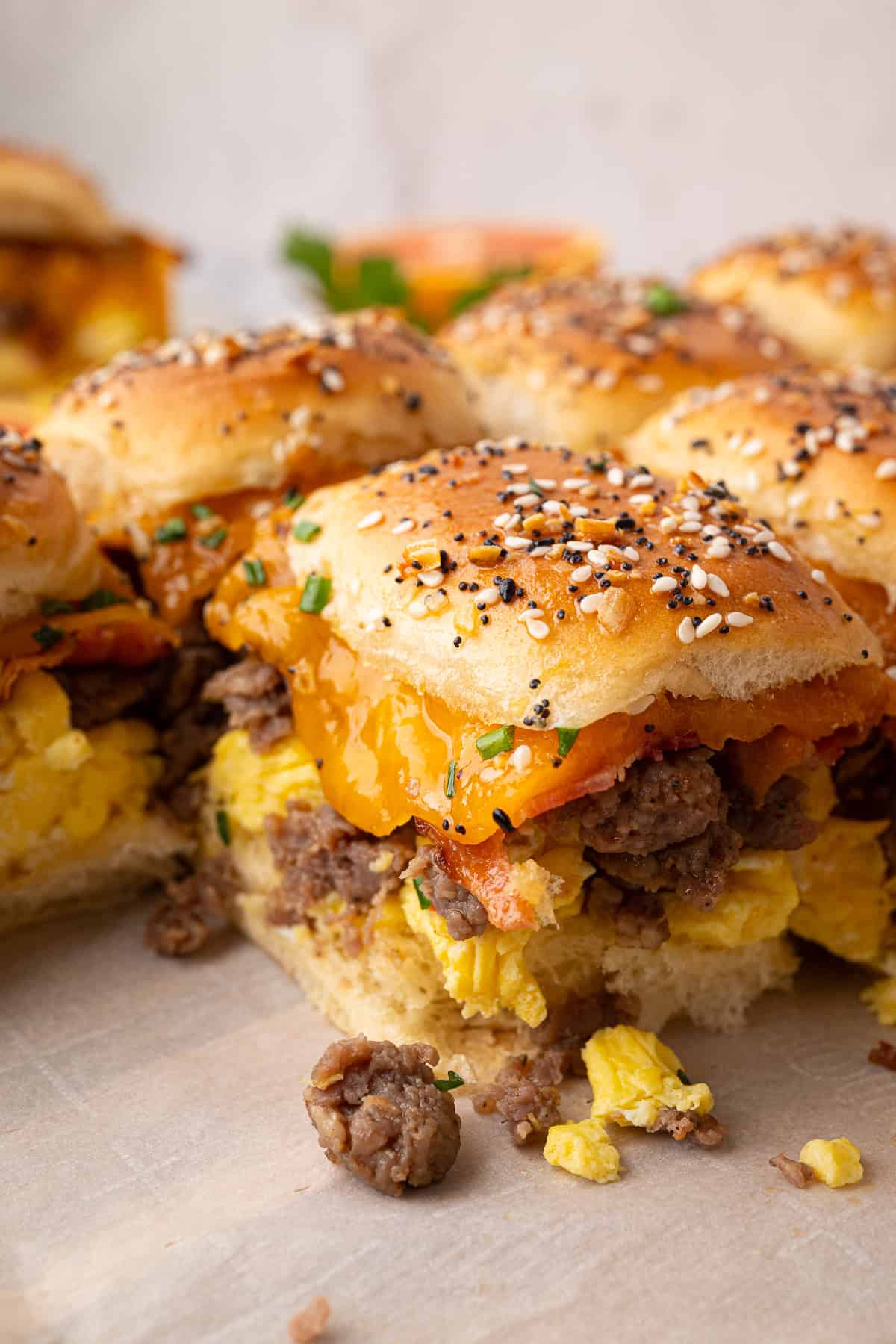 Breakfast sliders with scrambled eggs, ground sausage, melted cheddar cheese, and everything bagel seasoned buns, arranged on parchment paper.