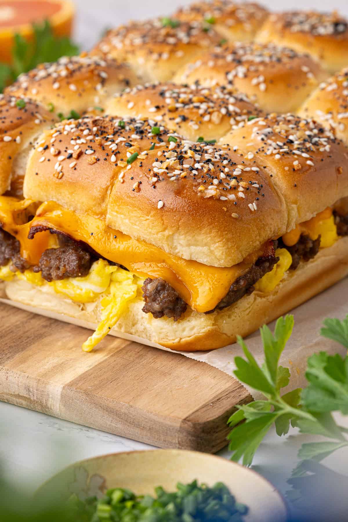 A close-up of breakfast sliders with scrambled eggs, sausage, and melted cheddar cheese on seeded slider buns, arranged on a wooden board.