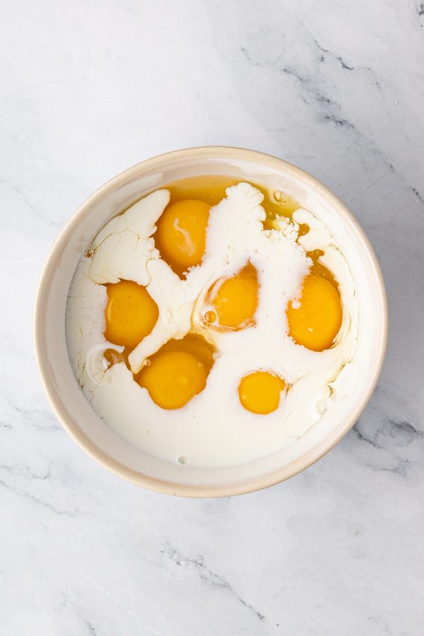 A bowl containing six raw eggs and milk on a white marble surface.