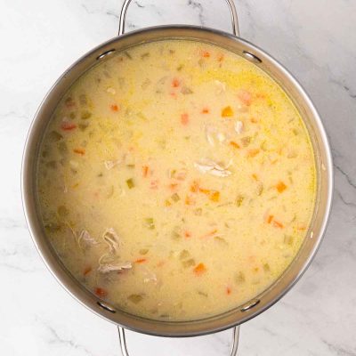 A stainless steel pot filled with creamy chicken and vegetable soup, featuring visible pieces of carrots, celery, and shredded chicken on a marble countertop.
