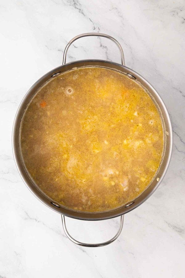 A large stainless steel pot filled with simmering broth or soup on a white marble countertop.