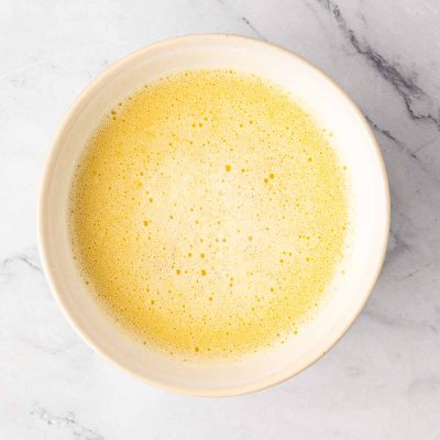 A white bowl filled with a frothy yellow liquid sits on a light marble surface.