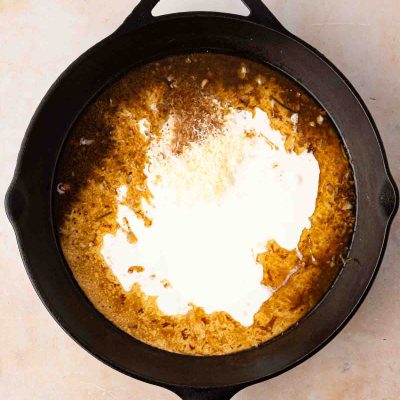 A black cast iron skillet containing a mixture of brown sauce and a swirl of cream, seen from above on a light countertop.