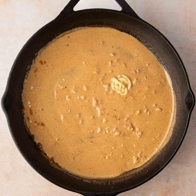 A cast iron skillet filled with a creamy brown sauce, sitting on a light-colored surface.