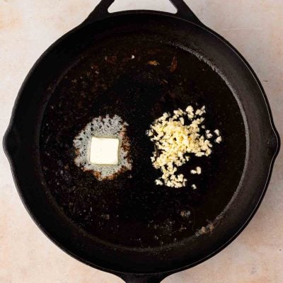 A cast iron skillet with a melting pat of butter and a pile of minced garlic on one side.