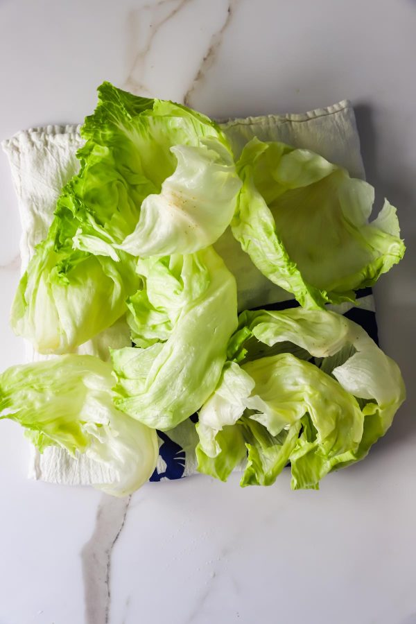 Several fresh iceberg lettuce leaves are arranged on a folded white cloth atop a marble surface.
