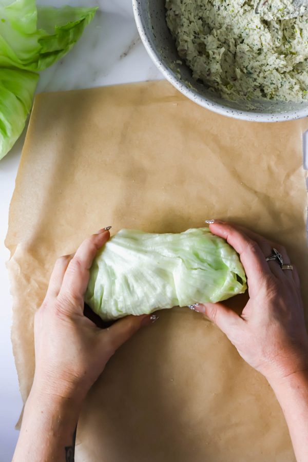 Hands rolling a lettuce leaf with filling on parchment paper; a bowl of the filling mixture is visible in the background.