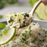 A close-up of a spoonful of cilantro lime cauliflower rice held above a plate, garnished with lime and fresh cilantro.