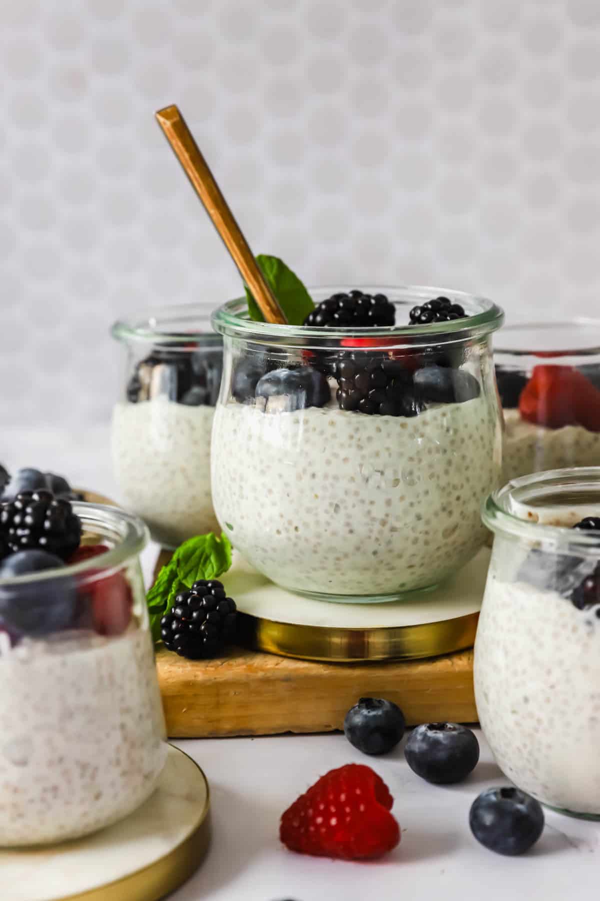 Glass jars filled with chia pudding topped with blackberries, blueberries, and raspberries, with a gold spoon in one jar.