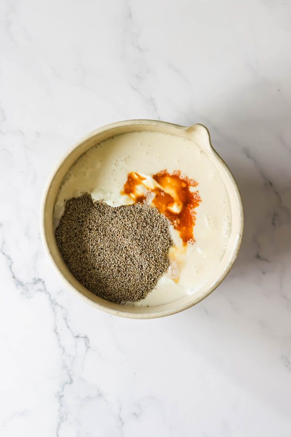 A mixing bowl on a marble surface containing a yogurt, chia seeds, and vanilla, not yet stirred together.