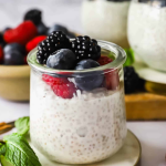Glass jar of chia seed pudding topped with fresh blackberries, raspberries, and blueberries, with mint leaves on the side.