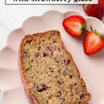 A slice of strawberry banana bread with strawberry glaze on a pink plate, garnished with fresh strawberry halves.