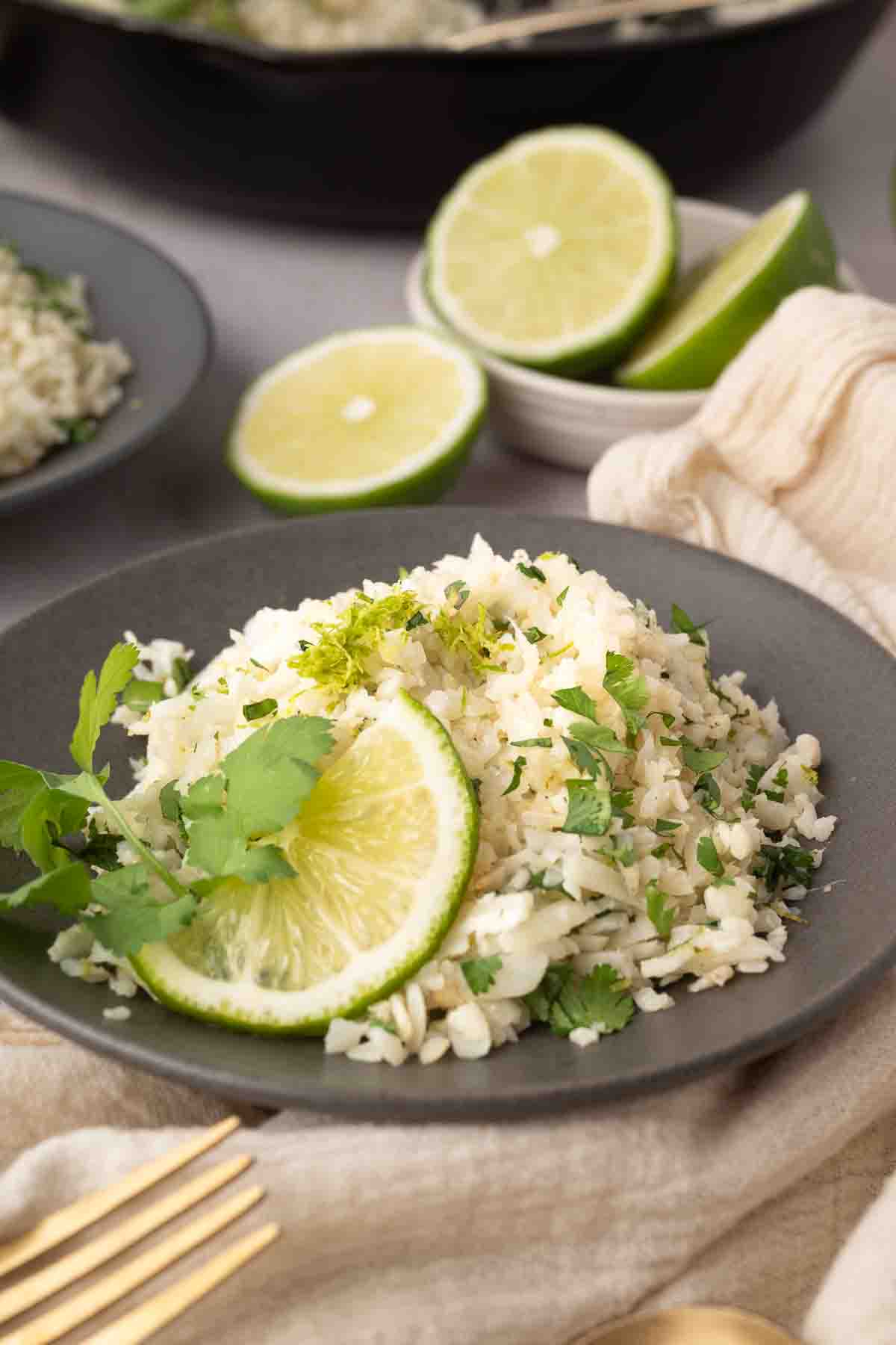 A plate of cilantro lime rice garnished with lime slices and fresh cilantro, with a halved lime and utensils nearby.