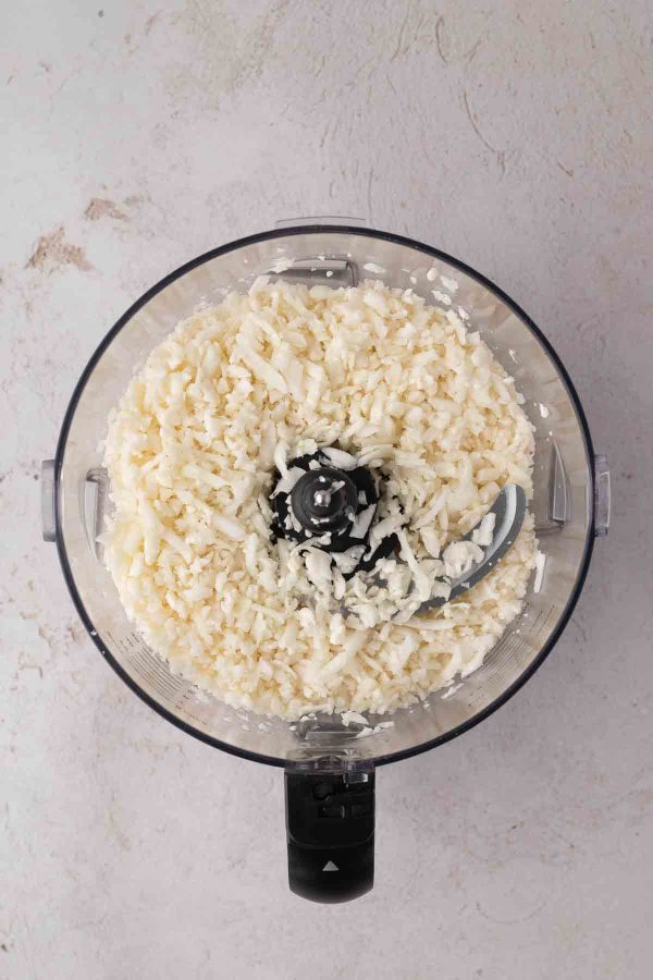 A food processor filled with freshly riced cauliflower on a light-colored countertop.