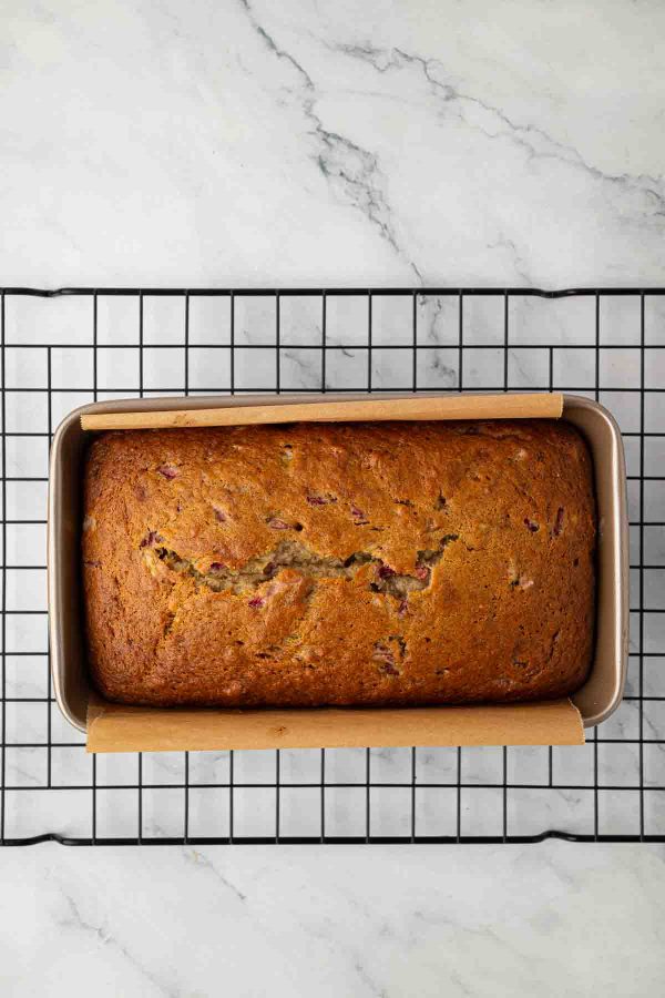 A loaf of baked bread in a rectangular pan, resting on a cooling rack over a white marble surface.